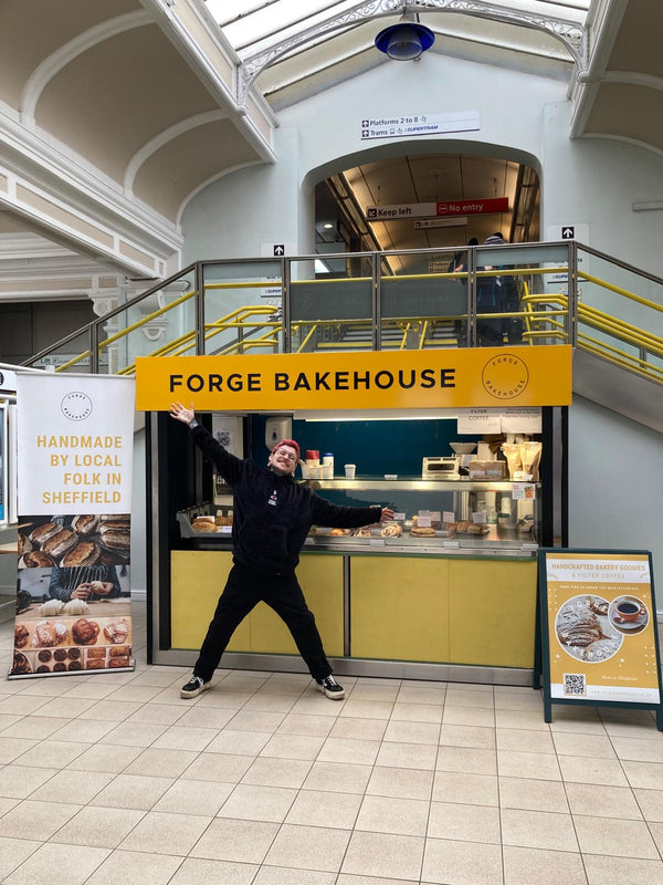 Person posing in front of Forge Bakehouse stand inside Sheffield Train Station